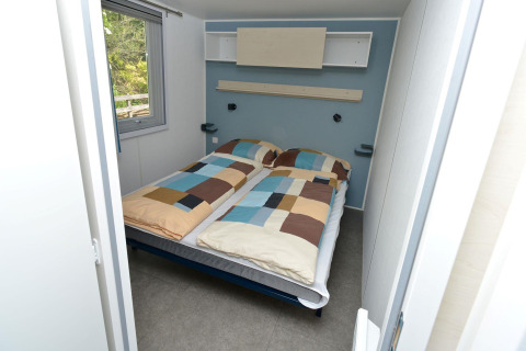 Slaapkamer in een mobilhome bij Drau Camping Sachsenburg in Oostenrijk met dubbel bed en raam.