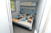 Slaapkamer in een mobilhome bij Drau Camping Sachsenburg in Oostenrijk met dubbel bed en raam.