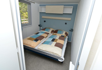 Slaapkamer in een mobilhome bij Drau Camping Sachsenburg in Oostenrijk met dubbel bed en raam.