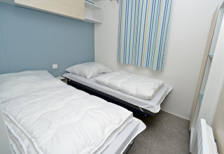 Twee eenpersoonsbedden in een compacte mobilhomekamer met gestreepte gordijnen bij Drau Camping Sachsenburg.