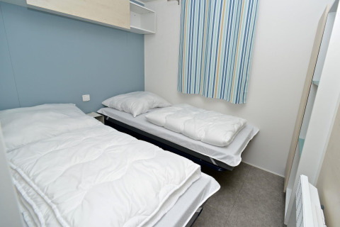 Dos camas individuales en una habitación compacta de casa móvil con cortinas a rayas en Drau Camping Sachsenburg.