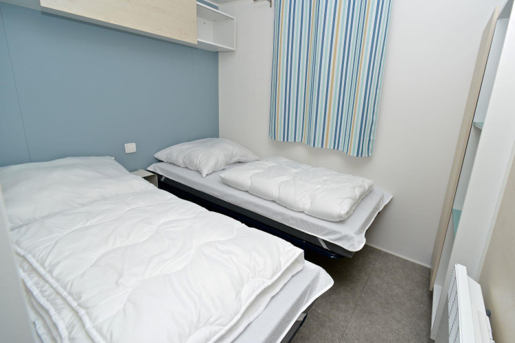 Dos camas individuales en una habitación compacta de casa móvil con cortinas a rayas en Drau Camping Sachsenburg.