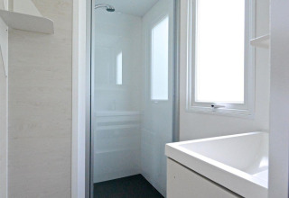 Lichte, moderne badkamer met douche en groot raam in een mobilhome bij Drau Camping Sachsenburg, Oostenrijk.