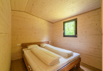Slaapkamer met houten wanden en tweepersoonsbed bij Wood Cubes op Drau Camping Sachsenburg, Oostenrijk.