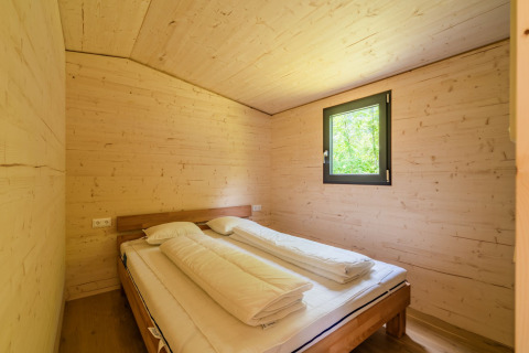 Slaapkamer met houten interieur en dubbel bed bij Wood Cubes, Drau Camping Sachsenburg in Oostenrijk.
