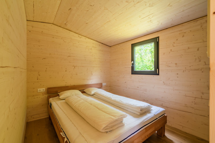 Slaapkamer met houten wanden en tweepersoonsbed bij Wood Cubes op Drau Camping Sachsenburg, Oostenrijk.