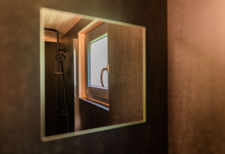 Spiegelbeeld van douche en raam in een moderne lodge bij Wood Cubes, Drau Camping Sachsenburg, Oostenrijk.
