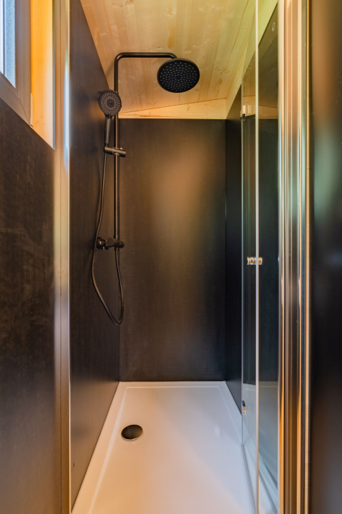 Cabina de ducha moderna con cabezal negro en un lodge de madera en Wood Cubes, Drau Camping Sachsenburg, Austria.