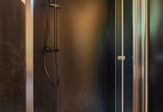 Cabina de ducha moderna con cabezal negro en un lodge de madera en Wood Cubes, Drau Camping Sachsenburg, Austria.