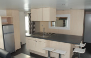 Cocina moderna en una casa móvil O'Hara en Camping Lac des Brenets, Suiza, con barra y taburetes blancos.