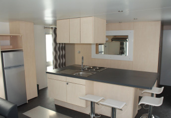 Cucina moderna in una casa mobile O'Hara al Camping Lac des Brenets, Svizzera, con isola e sgabelli bianchi.