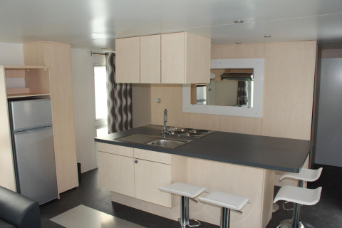 Cuisine moderne dans un mobil-home O'Hara au Camping Lac des Brenets, Suisse, avec ilot et tabourets blancs.