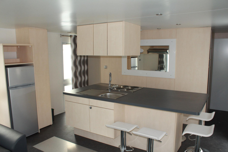 Cocina moderna en una casa móvil O'Hara en Camping Lac des Brenets, Suiza, con barra y taburetes blancos.