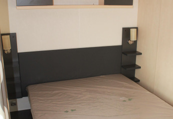 Camera da letto della casa mobile O'Hara al Camping Lac des Brenets, Svizzera, con letto e scaffali.