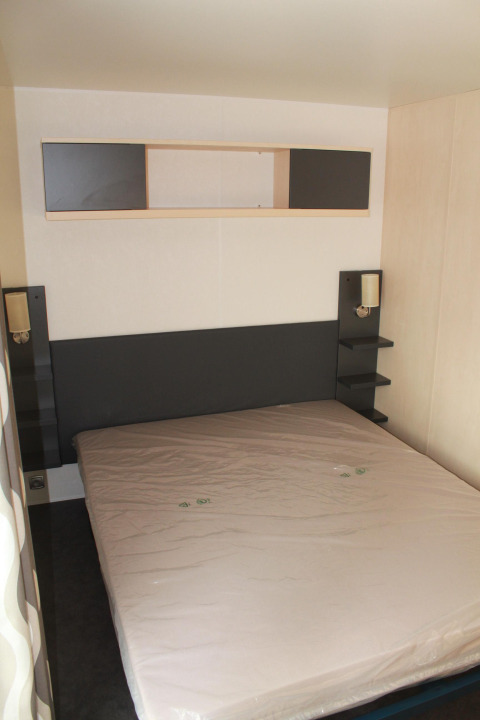 Dormitorio en Mobile home O'Hara en Camping Lac des Brenets, Suiza, con cama y estantes de almacenamiento.