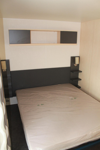 Chambre du mobile home O'Hara au Camping Lac des Brenets, Suisse, avec lit et étagères de rangement.