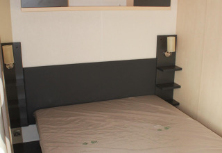 Chambre du mobile home O'Hara au Camping Lac des Brenets, Suisse, avec lit et étagères de rangement.