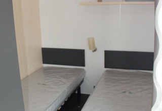 Habitación con dos camas individuales en una casa móvil en Camping Lac des Brenets, Suiza, con colchones nuevos.