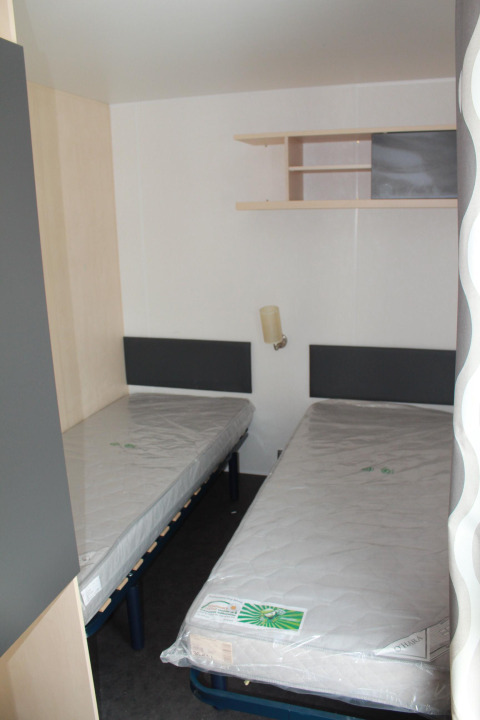 Habitación con dos camas individuales en una casa móvil en Camping Lac des Brenets, Suiza, con colchones nuevos.