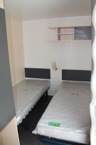 Bedroom with two single beds in a mobile home at Camping Lac des Brenets, Switzerland, with clean mattresses.