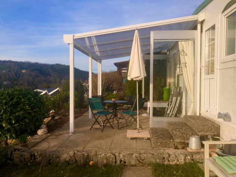 Sunny patio at Lavandou mobile home featuring table, chairs, umbrella, and a scenic hillside view.