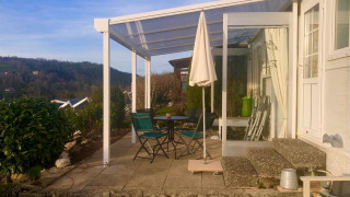Terrazza soleggiata al Lavandou mobile home con tavolo, sedie, ombrellone e vista sulle colline.