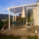Sunny patio at Lavandou mobile home featuring table, chairs, umbrella, and a scenic hillside view.