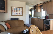 Interior de la casa móvil Lavandou en Camping Lac des Brenets, Suiza; cocina, sofá y mesa visibles.