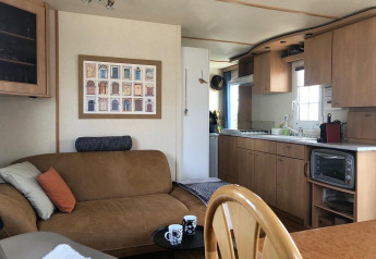 Interno della casa mobile Lavandou al Camping Lac des Brenets in Svizzera, con divano, cucina e tavolo.