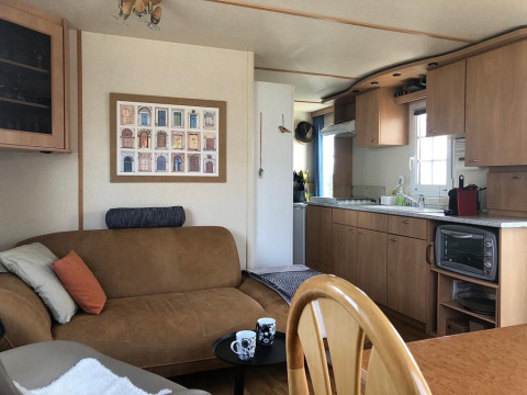 Indretning af Lavandou mobilhome ved Camping Lac des Brenets i Schweiz, med sofa, køkken og spisebord.