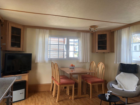 Lavandou mobile home at Camping Lac des Brenets, Switzerland, with dining area, TV, windows, and chairs.