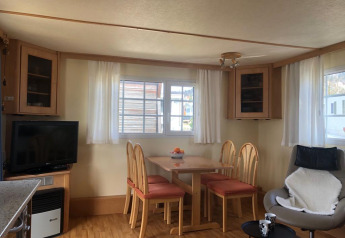 Wohnbereich im Lavandou-Mobilheim auf Camping Lac des Brenets in der Schweiz mit Esstisch und Fernseher.