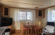 Lavandou mobile home at Camping Lac des Brenets, Switzerland, with dining area, TV, windows, and chairs.