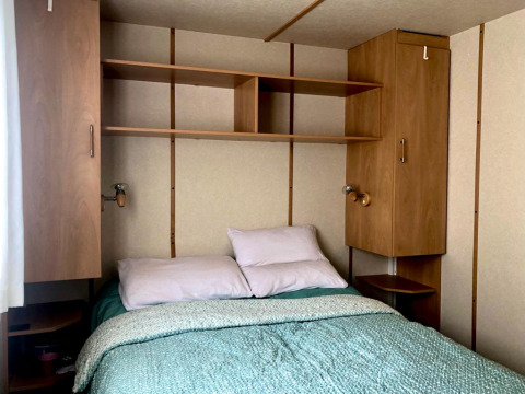 Camera da letto nella casa mobile Lavandou al Camping Lac des Brenets, Svizzera, con letto e armadi.