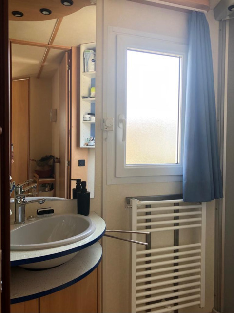 Bathroom in Lavandou mobile home at Camping Lac des Brenets, Switzerland, with sink and window view.