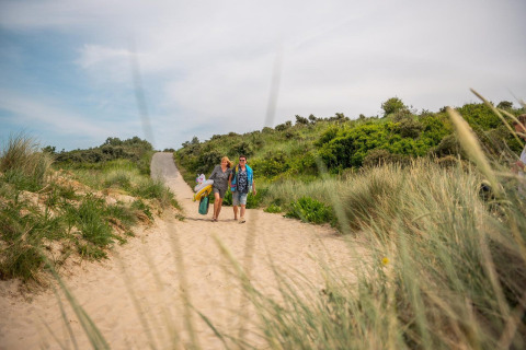 Two people walk through sandy dunes with beach gear near Cube Exclusif, EuroParcs De Zeeuwse Duinen.