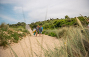 Due persone camminano tra le dune di sabbia con attrezzatura da spiaggia vicino Cube Exclusif, EuroParcs De Zeeuwse Duinen.