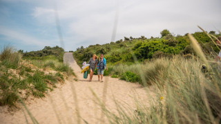 Zwei Personen spazieren mit Strandzubehör durch die Dünen bei Cube Exclusif, EuroParcs De Zeeuwse Duinen.