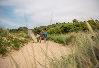 Dos personas caminan por dunas de arena con equipo de playa en Cube Exclusif, EuroParcs De Zeeuwse Duinen.