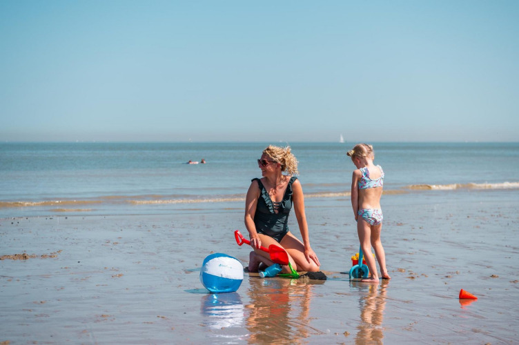 Eine Frau und ein Kind spielen mit Strandspielzeug am Wasser bei EuroParcs De Zeeuwse Duinen, Niederlande.