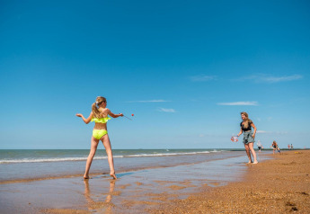 Twee personen spelen samen op het strand bij Cube Exclusif, EuroParcs De Zeeuwse Duinen, Nederland, onder blauwe hemel.