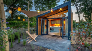 Kleine Wellness Suite Tiny House mit offener Glasfront, gemütlichem Garten und Lichterketten bei Sonnenuntergang.