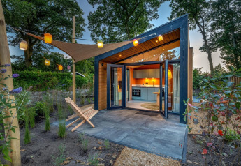 Casa diminuta Tiny Wellness Suite con puertas acristaladas abiertas, jardín y faroles colgantes al atardecer.