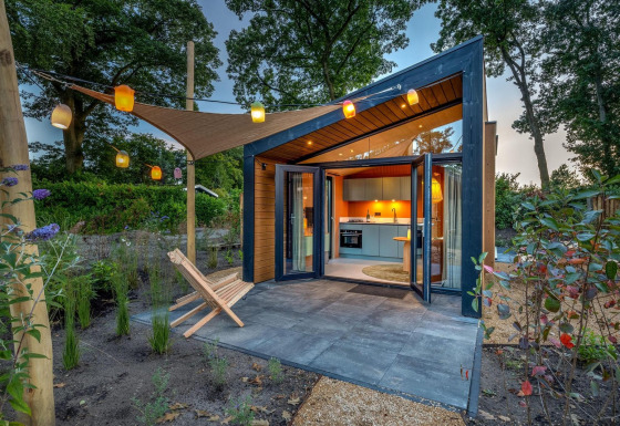 Casa diminuta Tiny Wellness Suite con puertas acristaladas abiertas, jardín y faroles colgantes al atardecer.