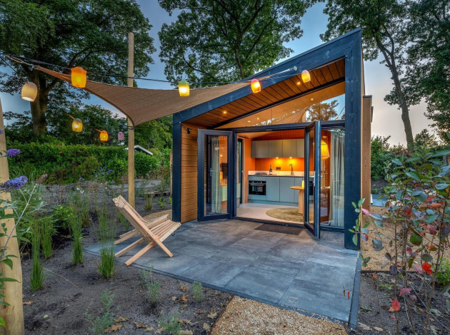 Tiny Wellness Suite, modern tiny house met openslaande deuren, tuin, zitje en sfeervolle lampions in de avond.