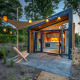 Moderne tiny house Tiny Wellness Suite med åbne døre, have og lanterner i smukke omgivelser om aftenen.