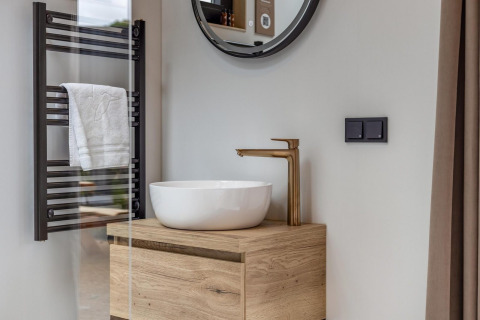 Modernes Badezimmer in der Tiny Wellness Suite im Holiday Park De IJsvogel, mit runder Spiegel und Holzwaschtisch.