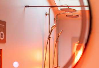 Shower and rainfall showerheads in the Tiny Wellness Suite at Holiday Park De IJsvogel, Netherlands, with warm lighting.