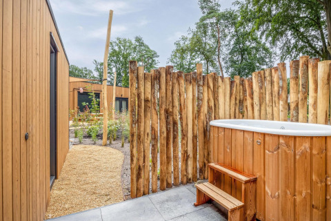 Udendørs wellnessområde med træbadekar, rustik afskærmning og moderne træhytter på Holiday Park De IJsvogel.