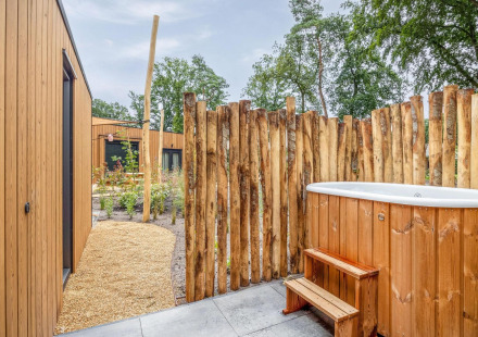 Buiten wellnessruimte met houten hottub, rustiek hek en moderne tiny houses op Holiday Park De IJsvogel.